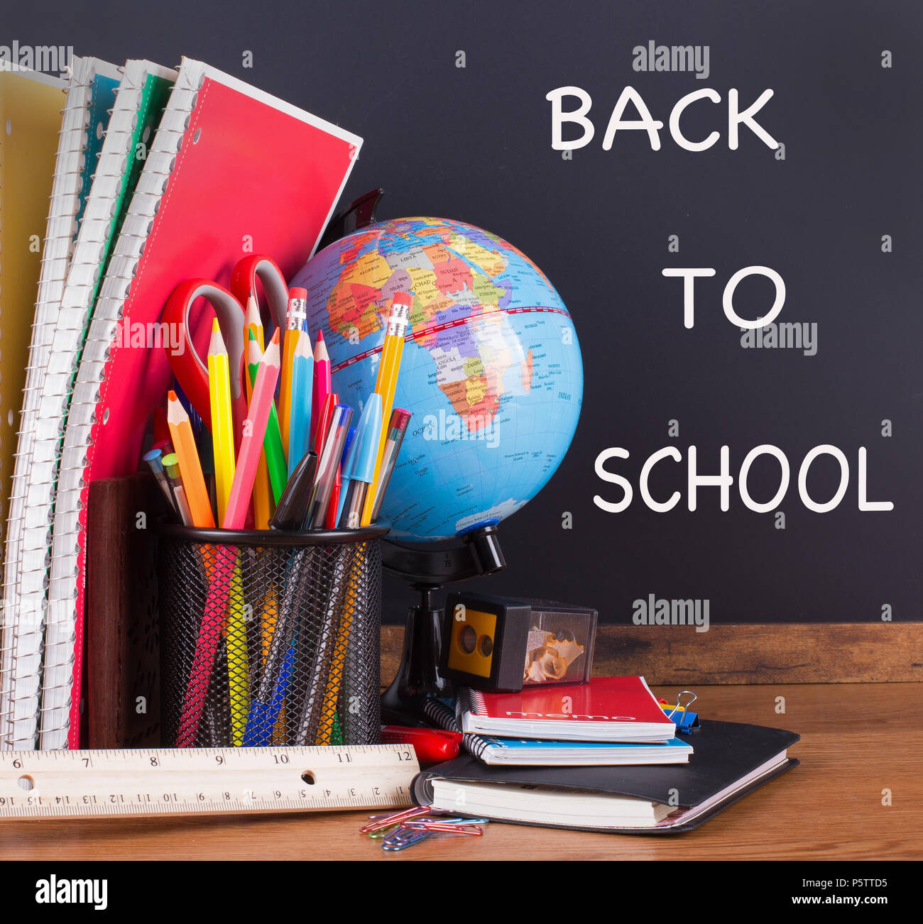 School accessories on a wooden desktop with BACK TO SCHOOL text written on a blackboard in background Stock Photo