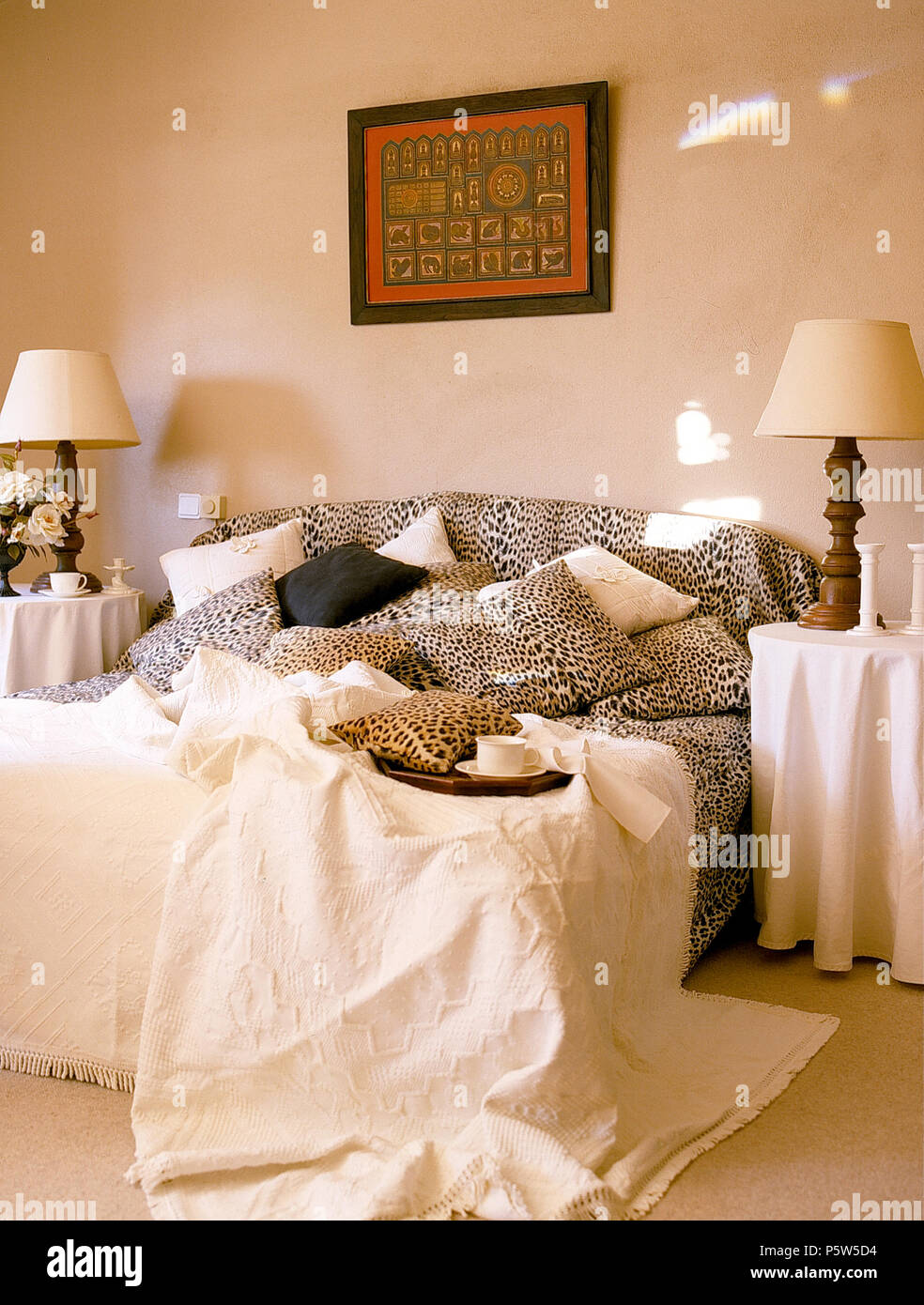 Bedroom with lamps on tables either side of double bed with leopard print bed linen and headboard with cream cotton bedspread Stock Photo