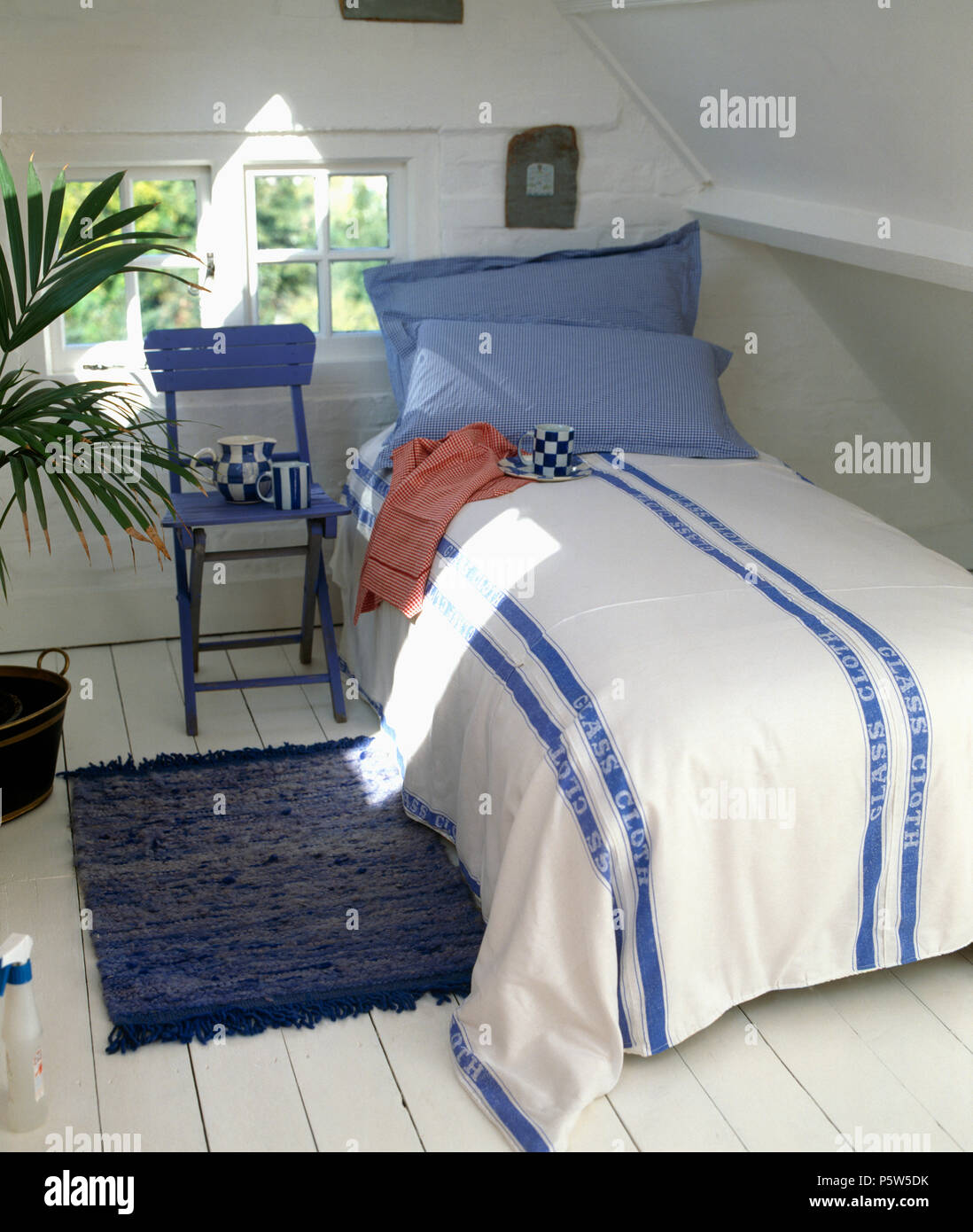 Bedcover made from blue striped white linen tea-towels on bed with blue pillows in simnple white attic bedroom Stock Photo