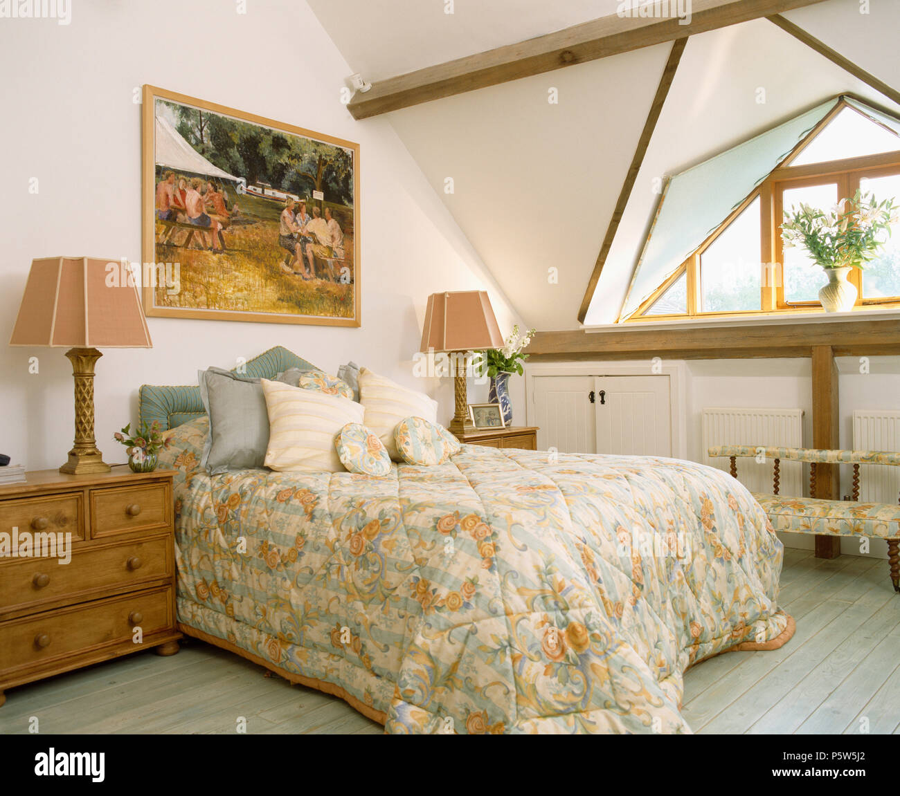 Lamps on pine chests-of-drawers either side of bed with floral quilt in attic country bedroom Stock Photo