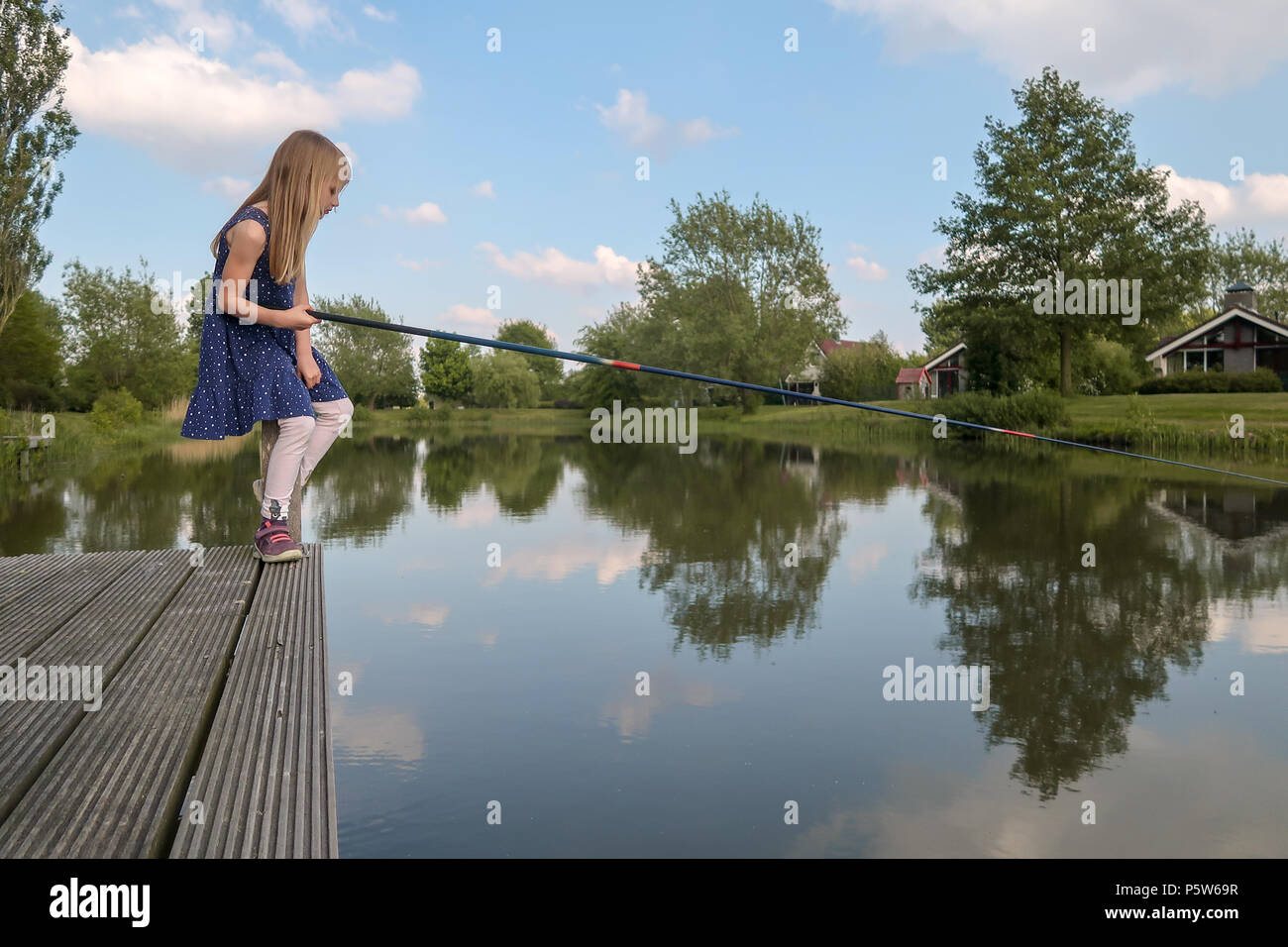A 7 year old girl is sitting by a lake with fishing rod and looking at the  water. She waits for a fish to bite Stock Photo - Alamy