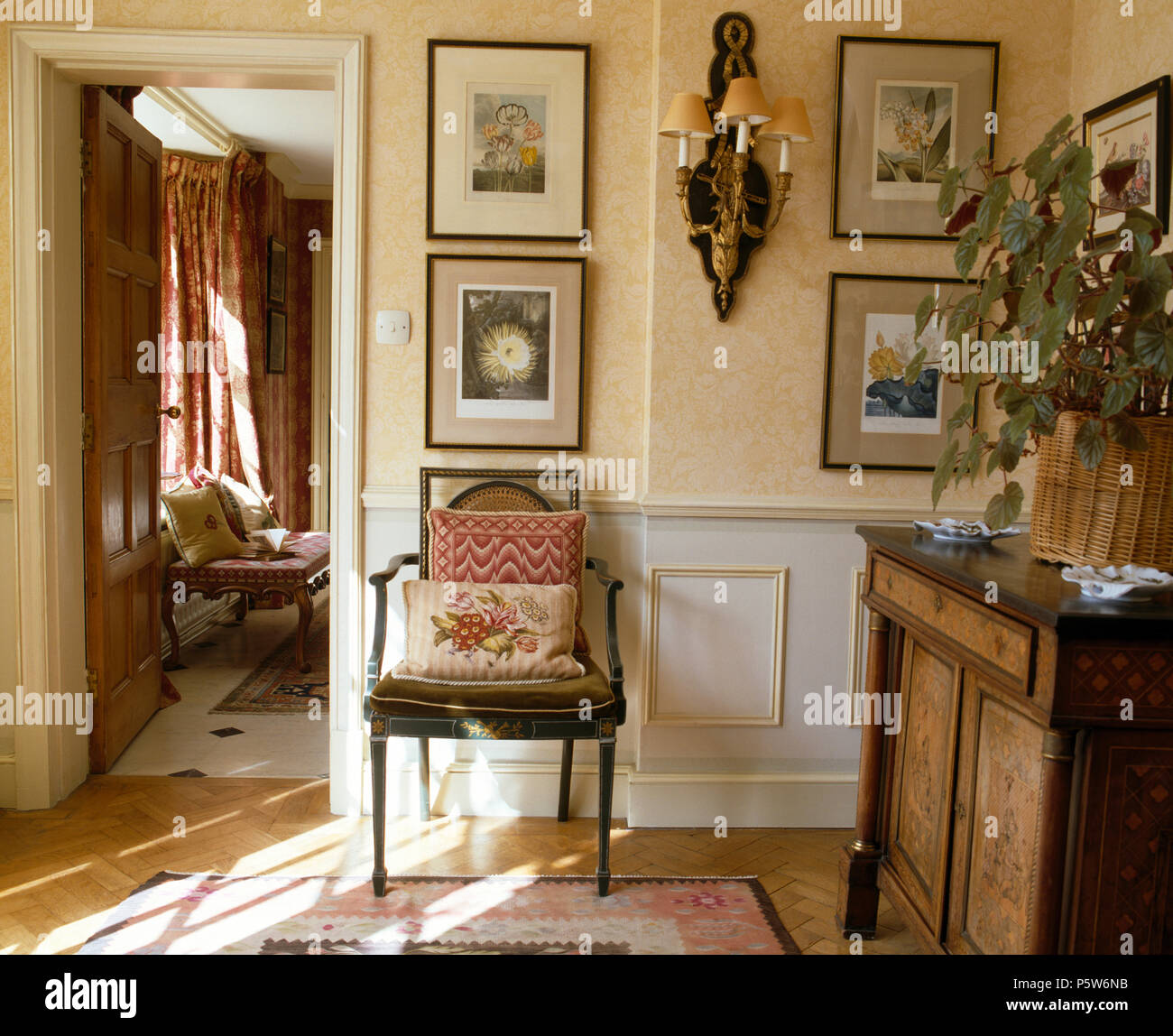 Antique chair and cupboard in cream hall with pictures on wall beside open doorway Stock Photo