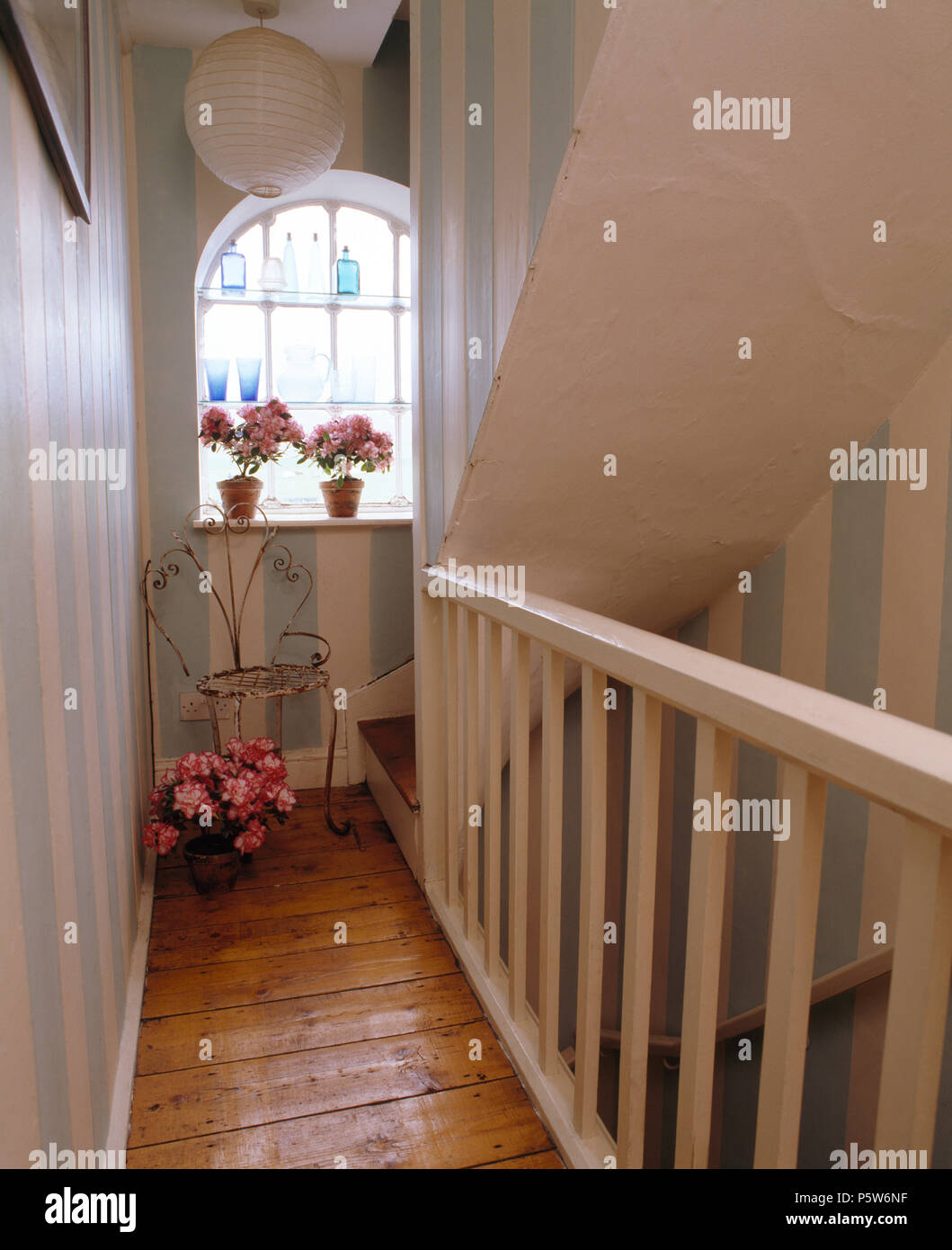 Hand painted blue+white stripes on walls of stairs and narrow landing with stripped wooden floorboards Stock Photo