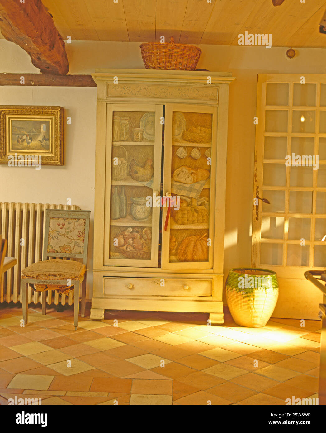 Trompe-l'oeil scene painted on doors of old cupboard in French country hall with large ceramic pot Stock Photo