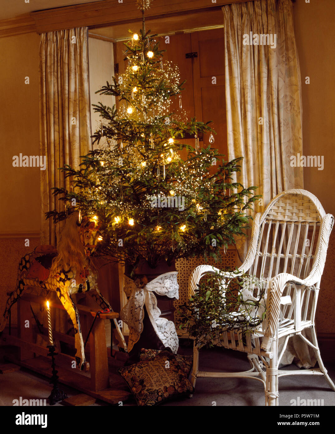 Rocking horse and white wicker chair either side of Christmas tree with simple decorations and lighting Stock Photo