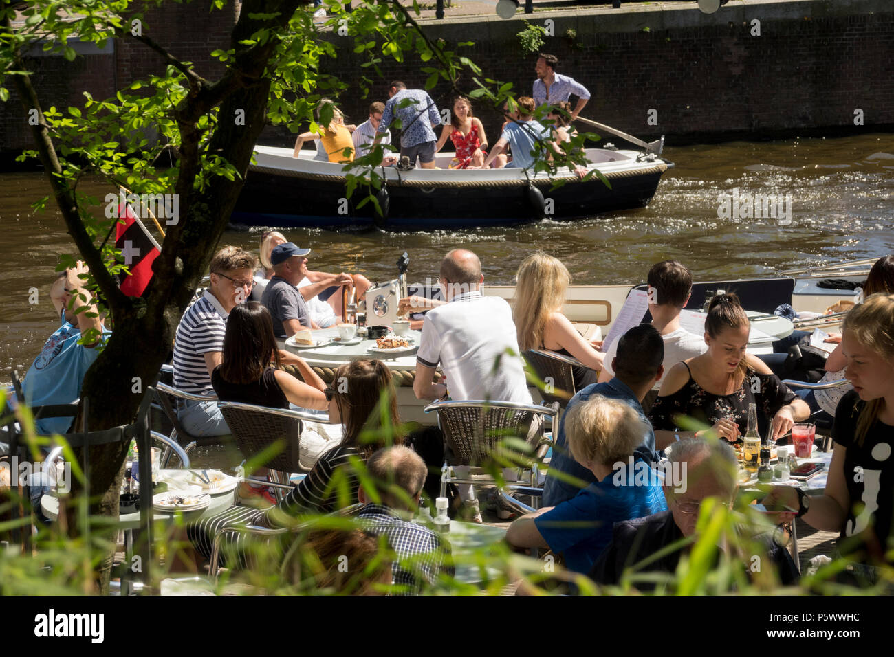 AMSTERDAM, NETHERLANDS - MAI 10, 2018: tourists take a drink in the sun on the terrace of a cafe on the banks of a canal in Amsterdam Stock Photo