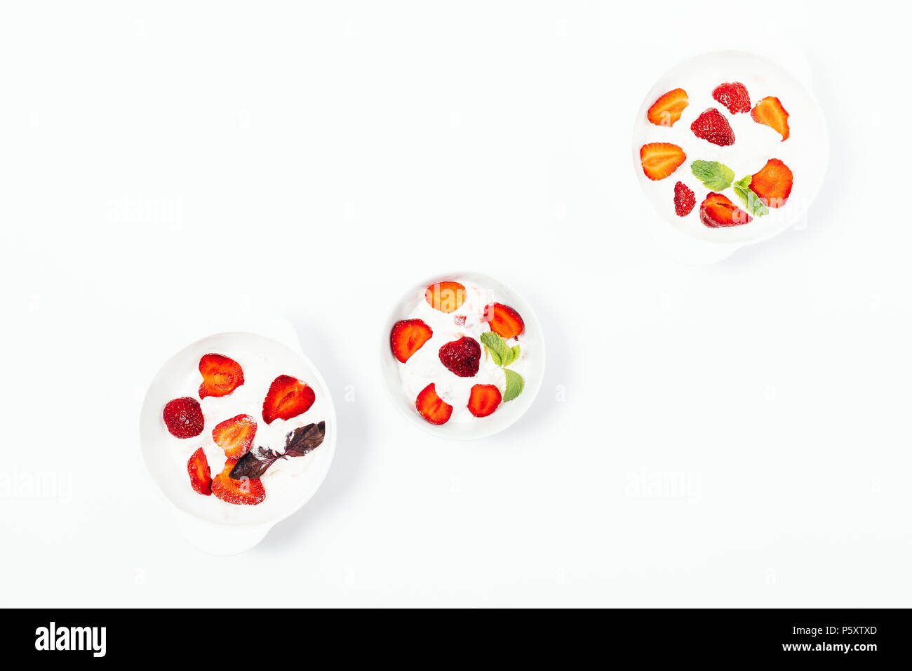 Three bowls of strawberry ice cream on a white table, top view. Flat lay composition of cold desserts decorated with fresh red berries and mint and pu Stock Photo