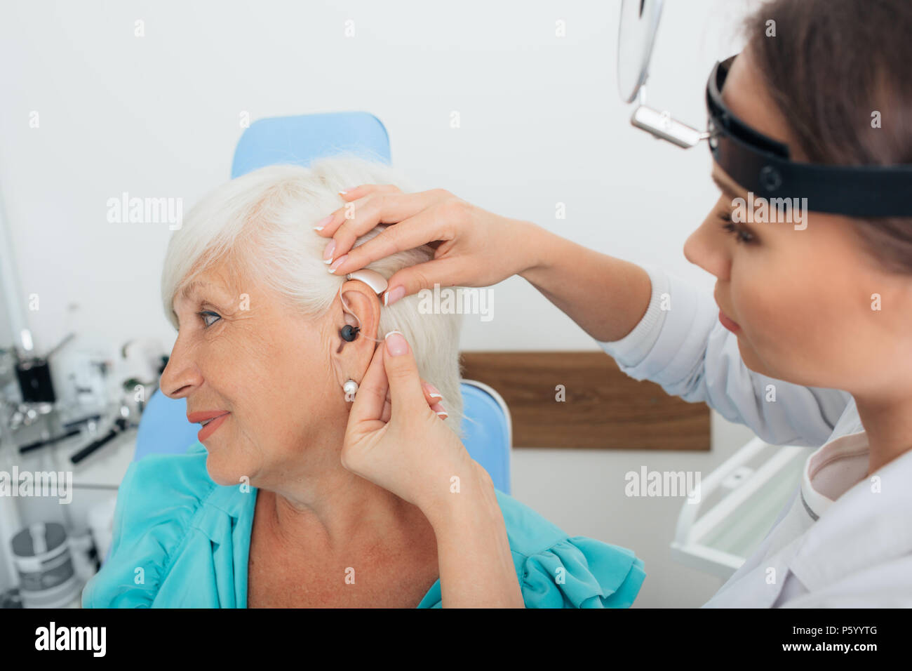 doctor helping elderly woman inserting hearing aid Stock Photo
