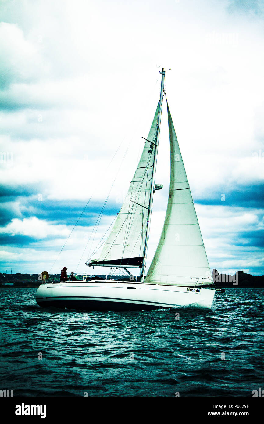 A yacht sailing in a harbour with the wind catching it's sails Stock