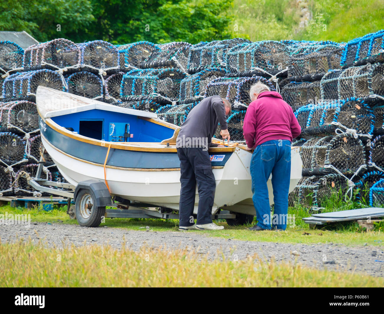 Two men carrying out a minor repair to a wooden fishing coble in front ...