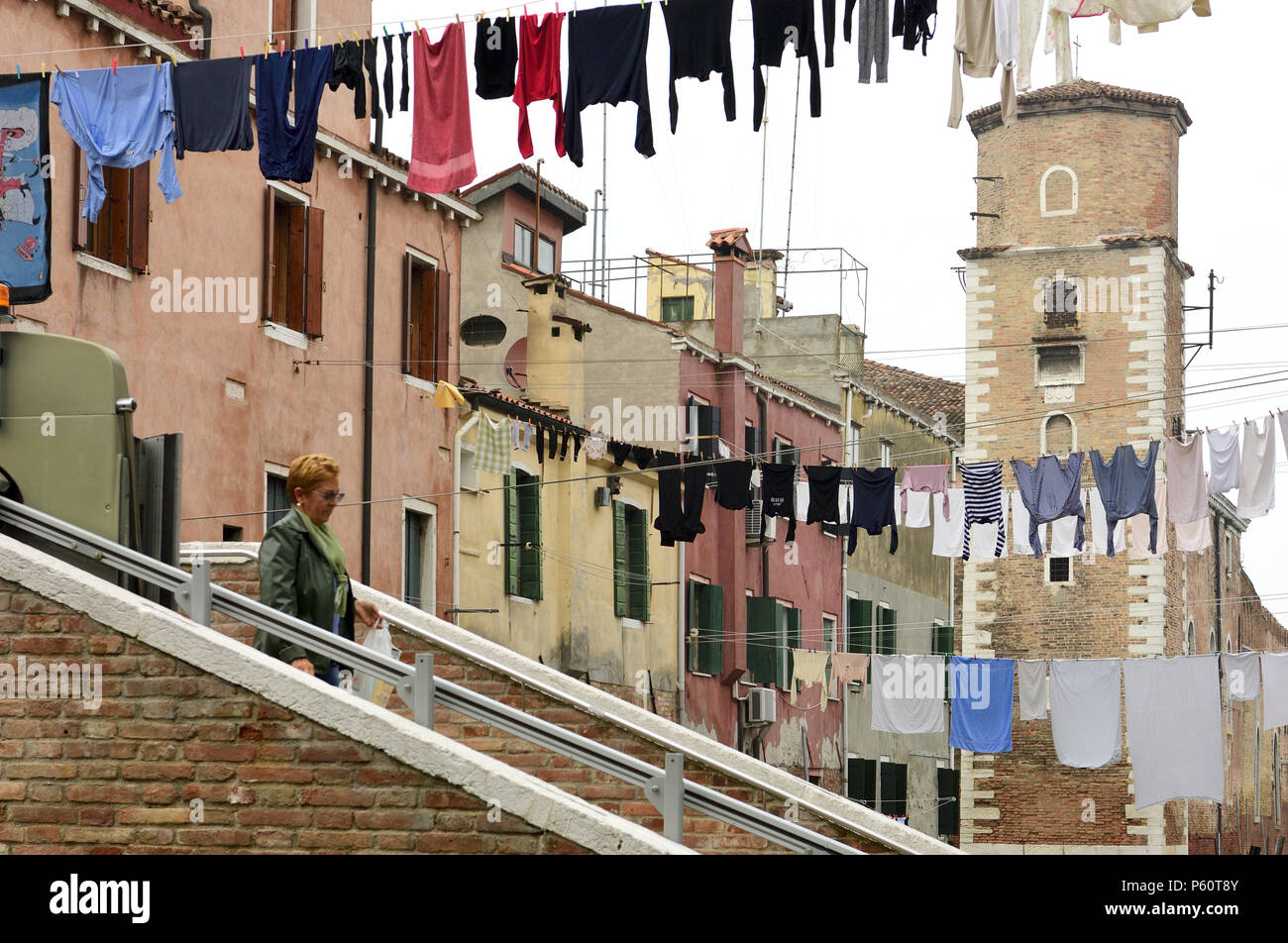 An Italian woman walks past hanging laundry in the off-beat residential neighborhoods of the Commune di Venezia and Centro Storico in Venice, Italy. Stock Photo