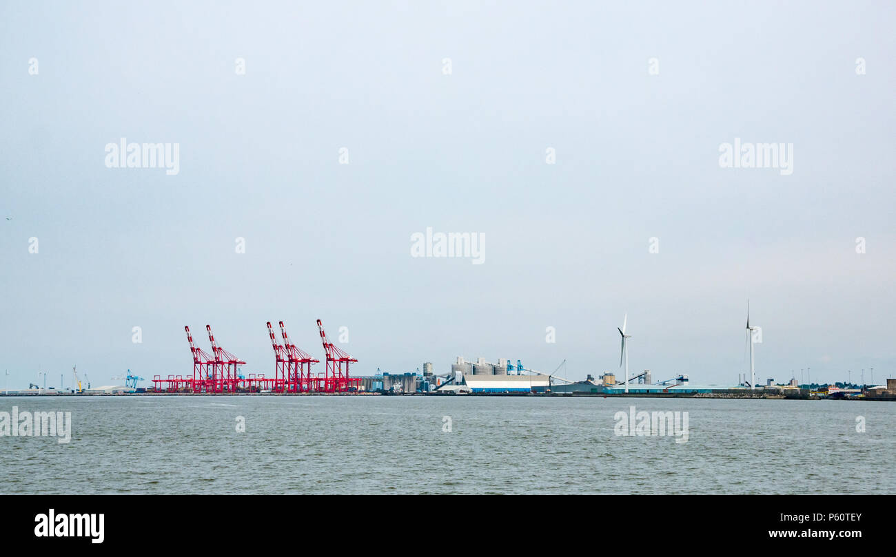 Distant view from from River Mersey of towering red cranes and wind turbines in dock area of Liverpool, England, UK Stock Photo
