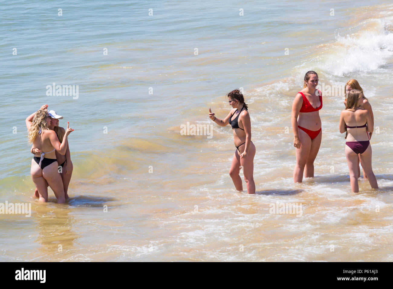 Bournemouth, Dorset, UK. 28th June, 2018. UK weather: sunseekers head to the beaches at Bournemouth on another hot sunny day with unbroken blue skies and sunshine. A slight breeze makes the heat more bearable. A group of friends in skimpy bikinis have fun playing in the sea and taking photos. Credit: Carolyn Jenkins/Alamy Live News Stock Photo
