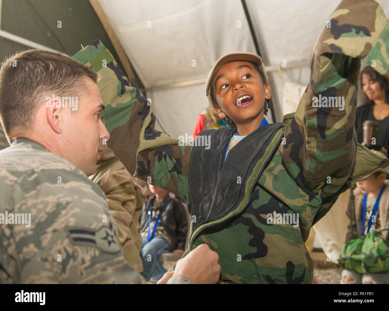 (HOLLOMAN AIR FORCE BASE, N.M.) Airman 1st Class Patrick O’Donnell, a 49th Civil Engineer Squadron specialist, assists Antonio Jones, 5, with putting on personal chemical protective gear during Operation K.I.D. (Kids Investigating Deployment), April 8 at Holloman Air Force Base, N.M. April is the Month of the Military Child. The Airmen and Family Readiness Center and Youth Center hosted Operation K.I.D. to expose military children to the different phases of deployment that their active duty family members go through. (U.S. Air Force photo by Staff Sgt. E’Lysia A. Wray/Released) Stock Photo