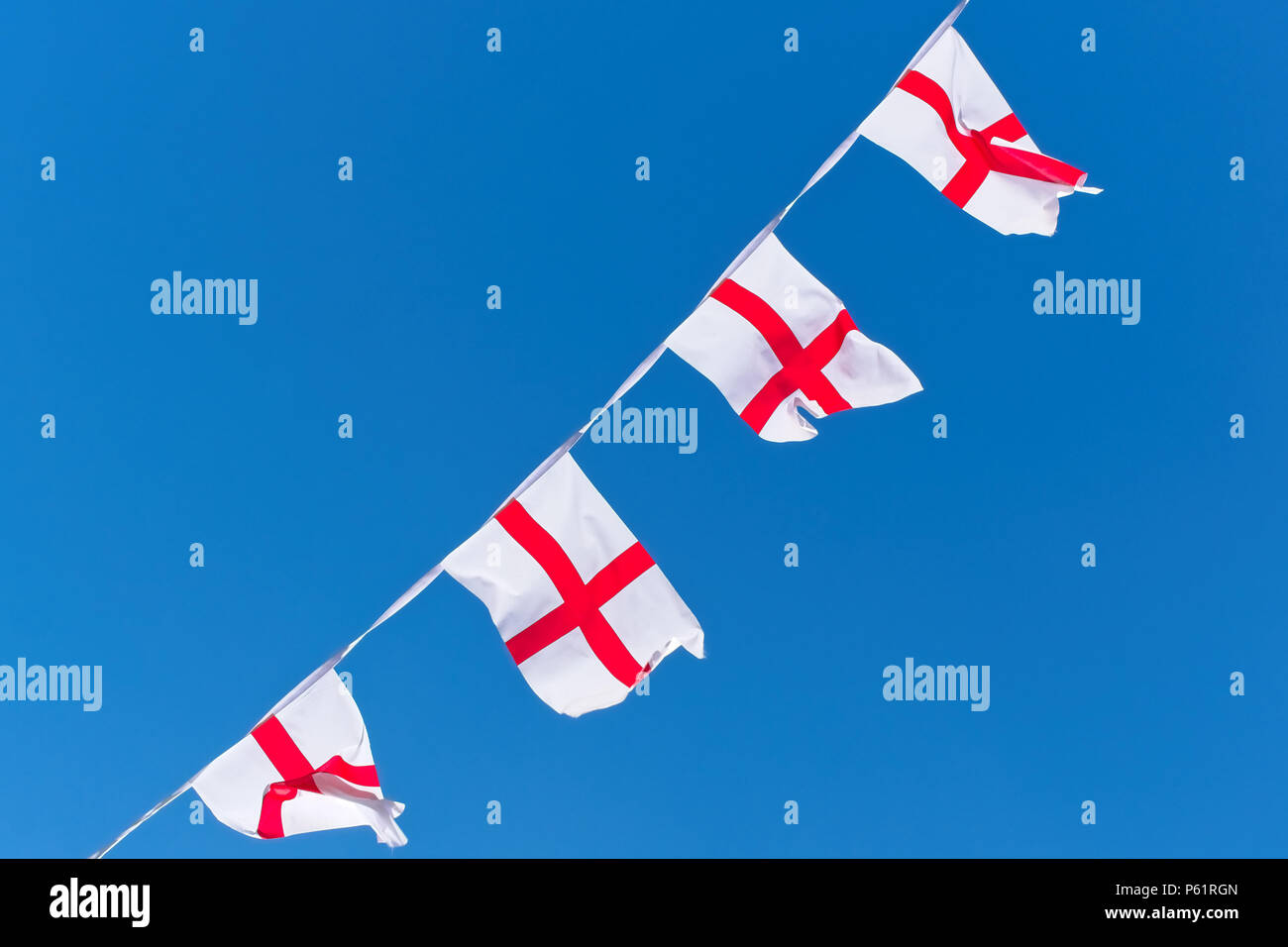 Single row of England flags / bunting flying against blue sky Stock