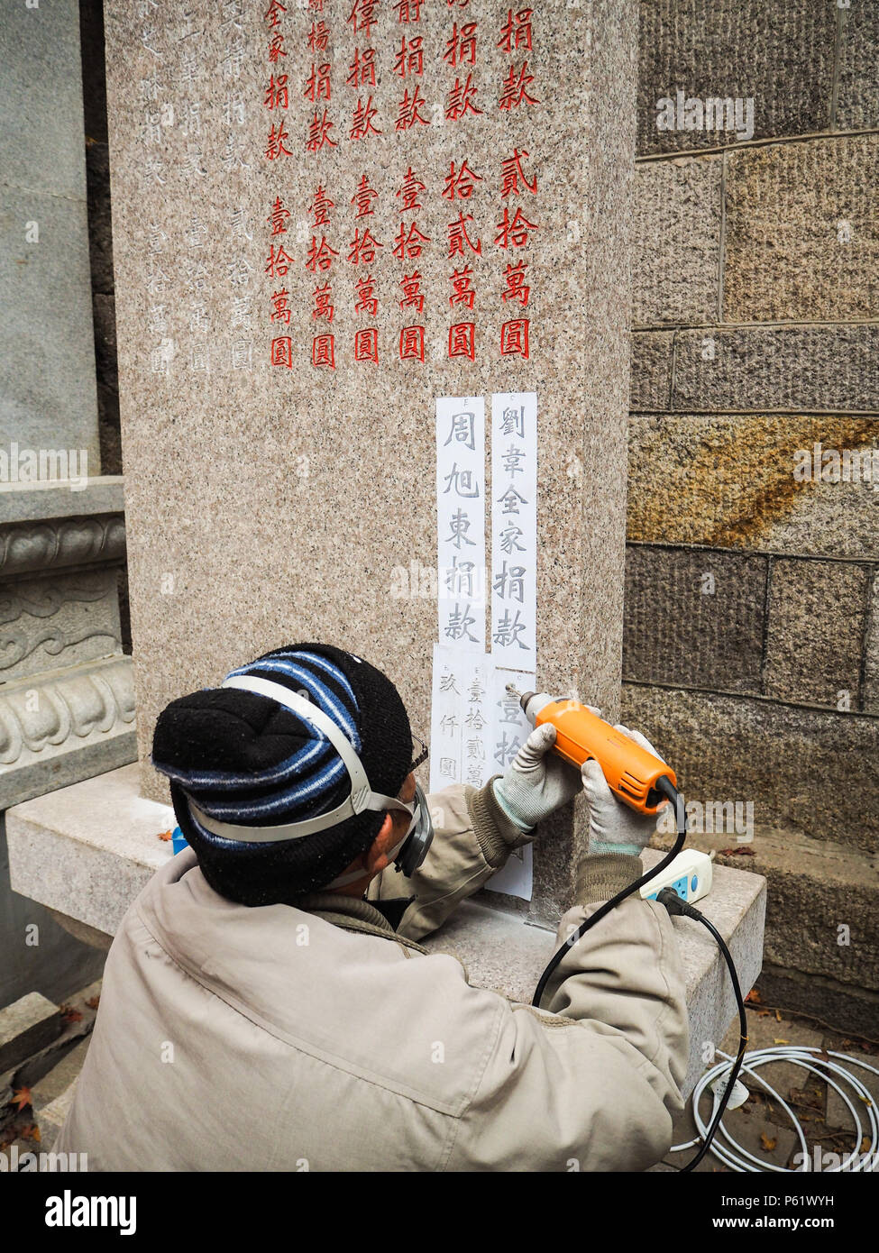 Qingdao, China - December 2017: Older man carving names and donation amount on s stele in Taiqing temple, Laoshan Stock Photo