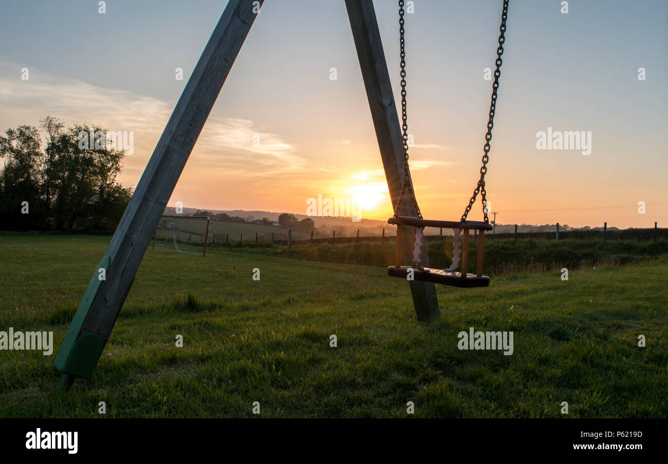 An unused swing in a children's park at sunset Stock Photo
