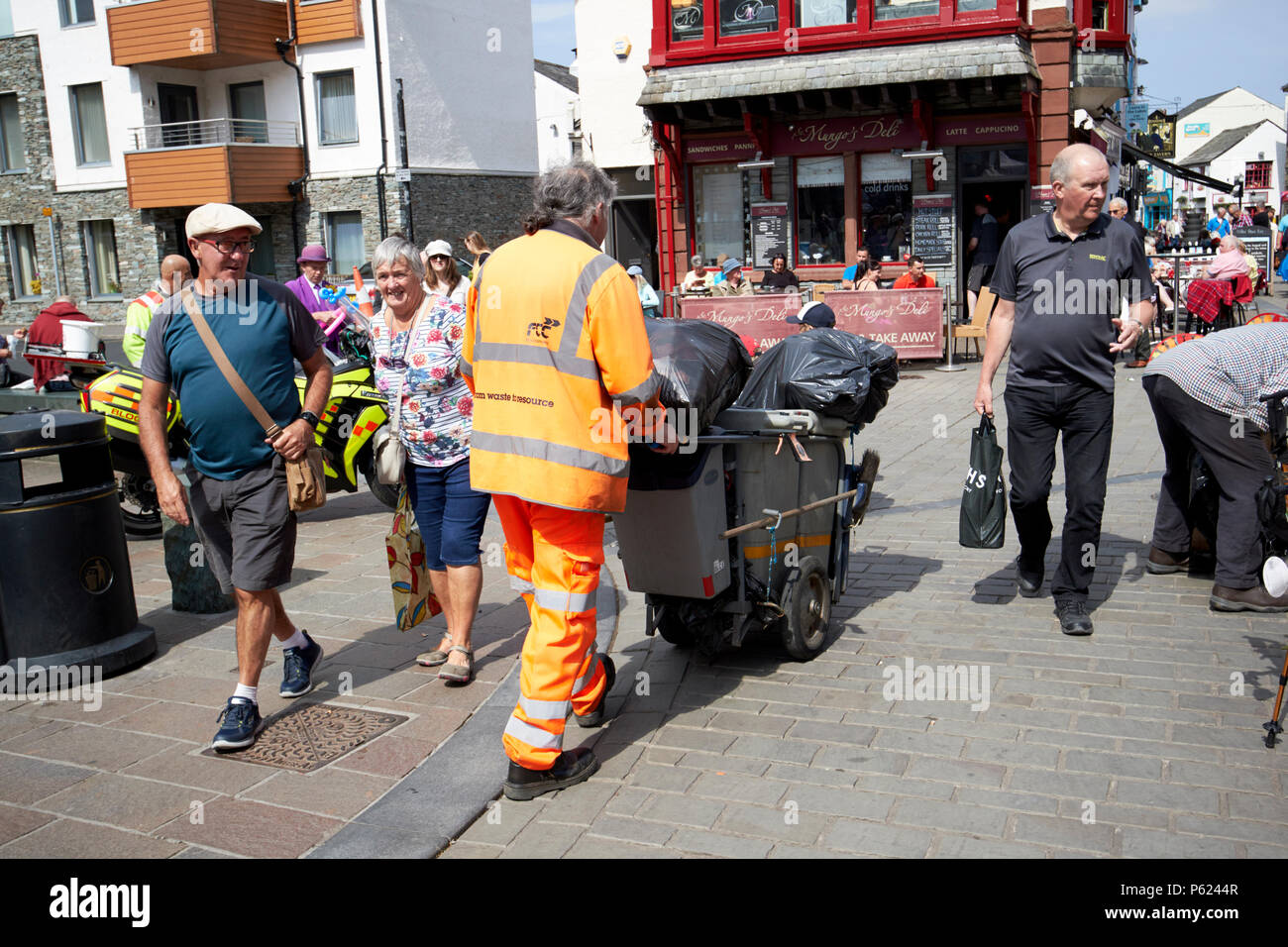 street cleaner wearing high visibility clothing pushing bin cart in Keswick Lake District Cumbria England UK Stock Photo