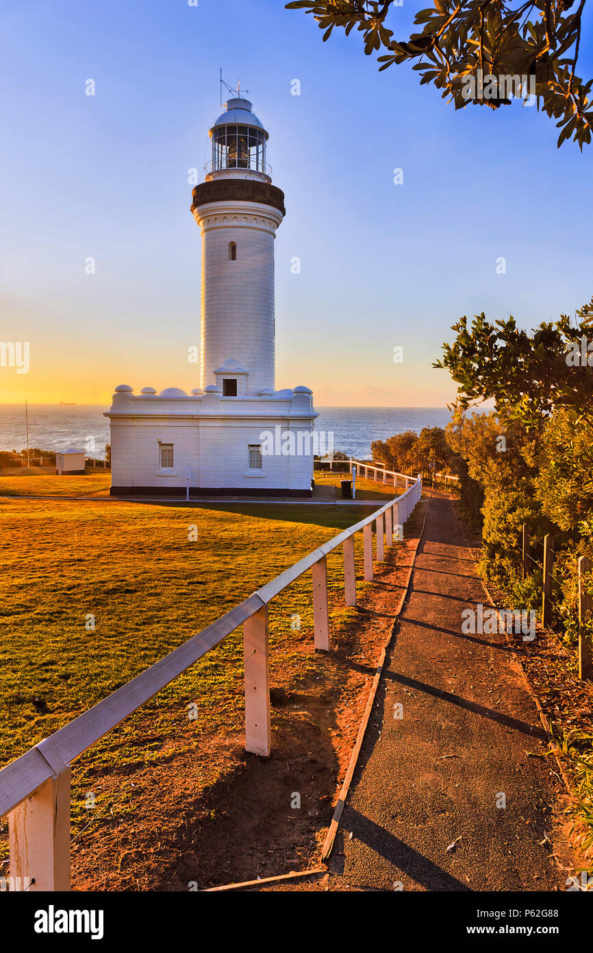 White stone Norah lighthouse on Norah head of Australian Central coast in warm light of rising sun agaist Pacific ocean with leadway. Stock Photo