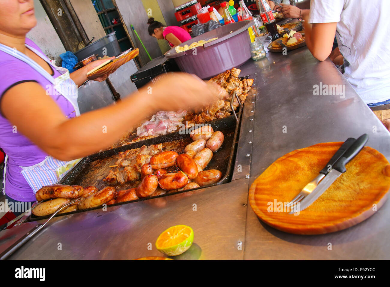 Local woman cooking meat for asado at Mercado 4 in Asuncion, Paraguay. Asado is a traditional dish in Paraguay and usually consists of beef alongside  Stock Photo