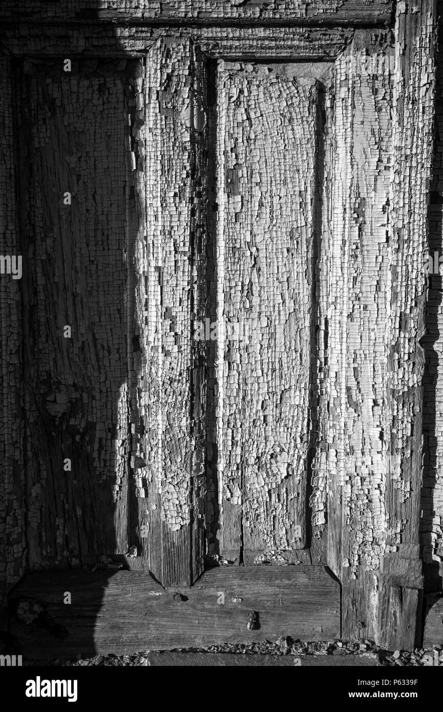 Weathered wooden door with chipped paint of an abandoned house in the village of Chavdar, Bulgaria. Black and white image, close-up on painting Stock Photo