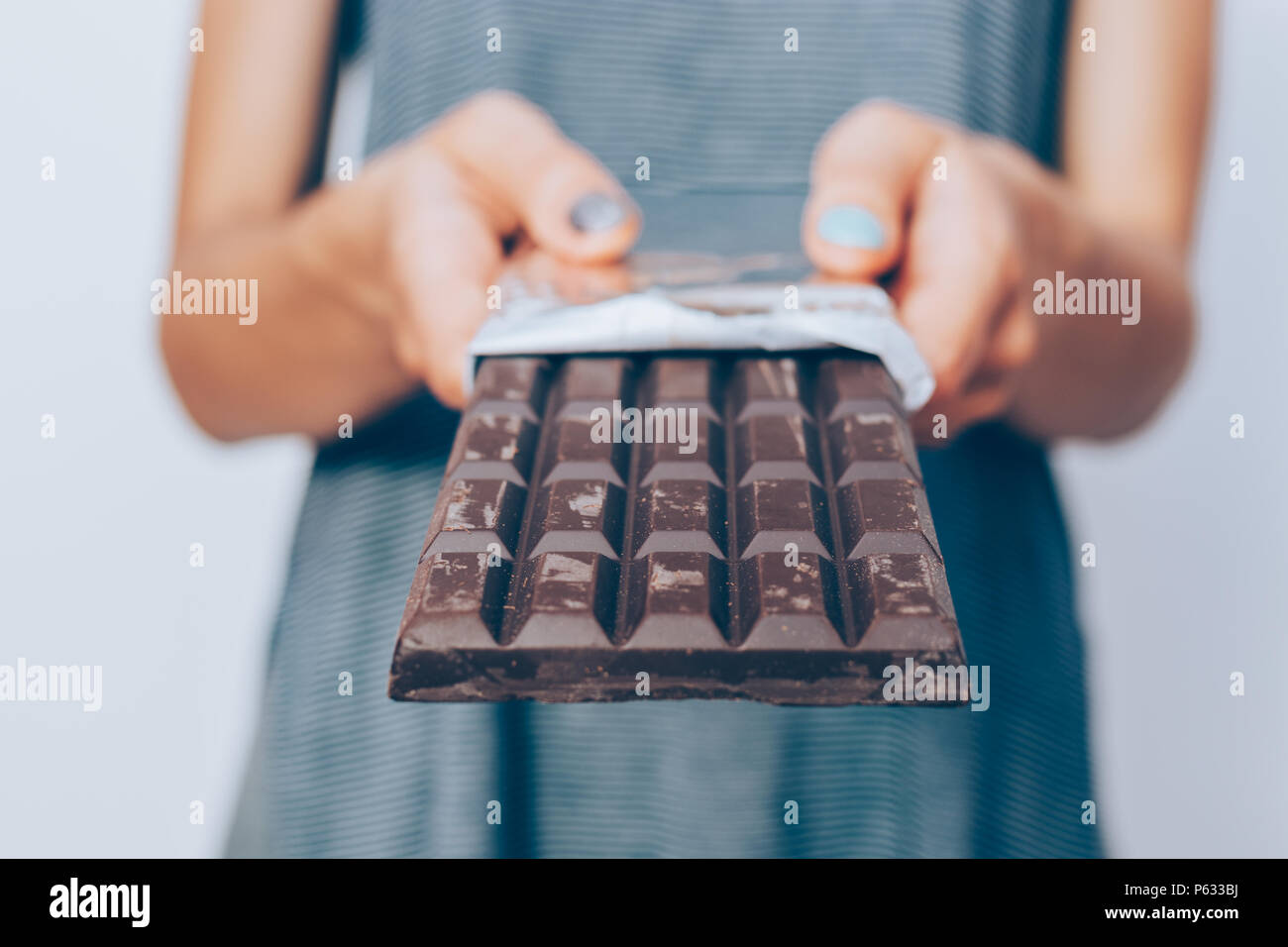 Woman's hands holding unwrapped dark chocolate bar, close-up. Unrecognizable female standing and giving dessert. Stock Photo