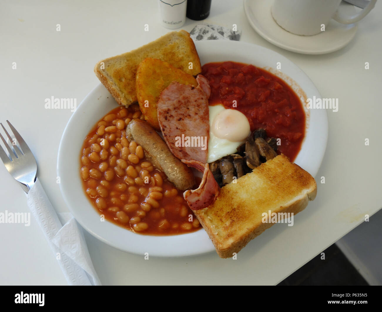 Full English all day Breakfast in a Sheffield cafe. Bacon, Egg, Tinned Tomatoes,Hash Browns, Beans, Sausage, Mushrooms with toast and of course a good Stock Photo