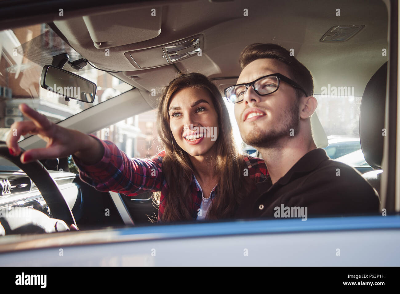 Enjoying travel. Beautiful young couple sitting on the front passenger seats and smiling while handsome man driving a car. Stock Photo