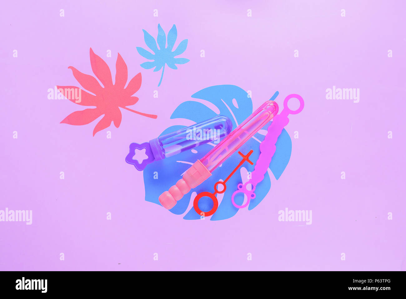 Bubble wands on a pastel purple background with tropical leaves and copy space. Summer flat lay header in pink. Stock Photo