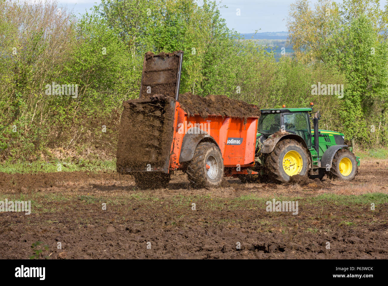A farmer using a manure spreader behind his tractor to spread an