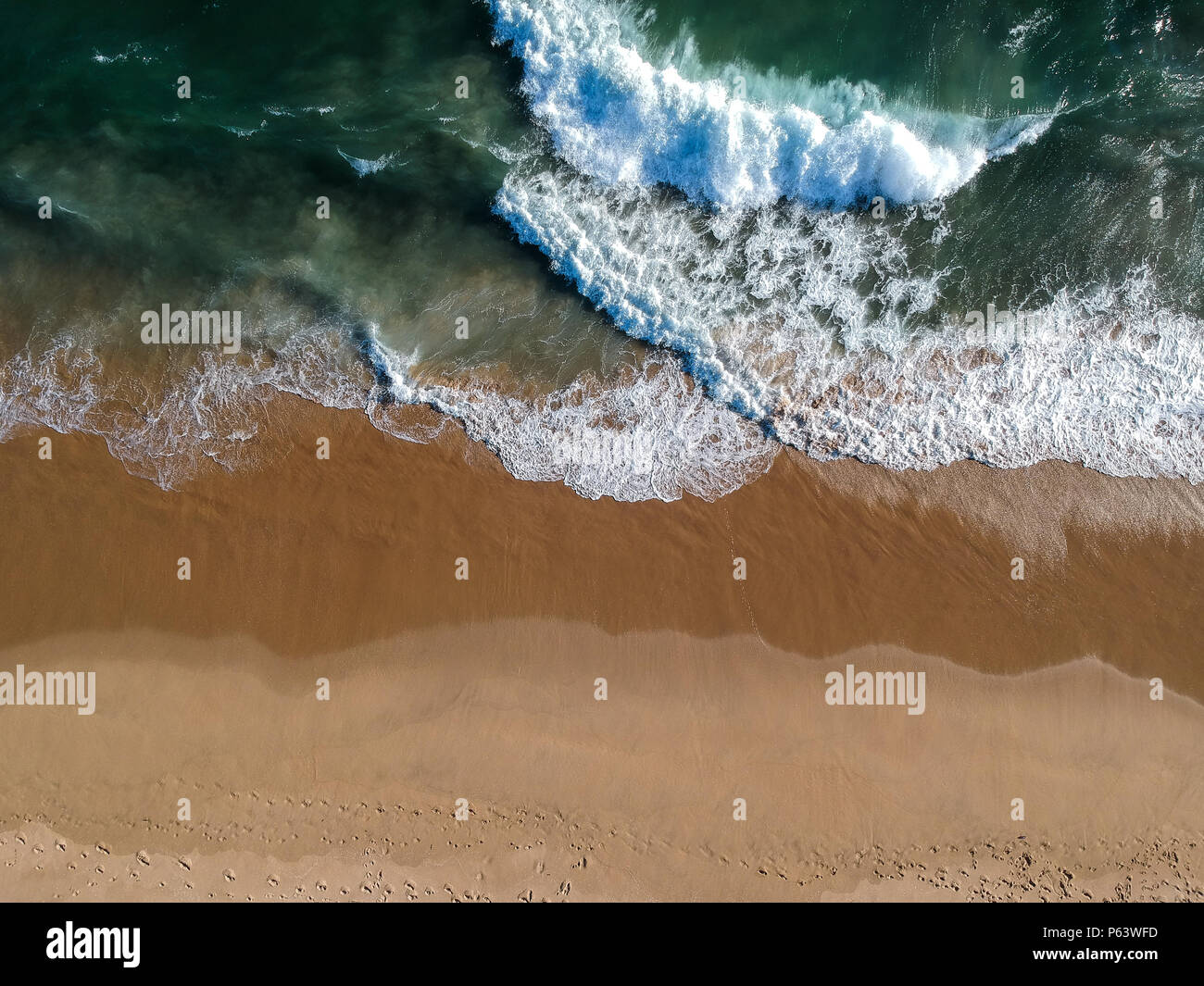 An aerial shot at 330 feet/100 meters looking down at the Pacific Ocean breaking along the Southern California Coast. Strong waves and currents leave  Stock Photo