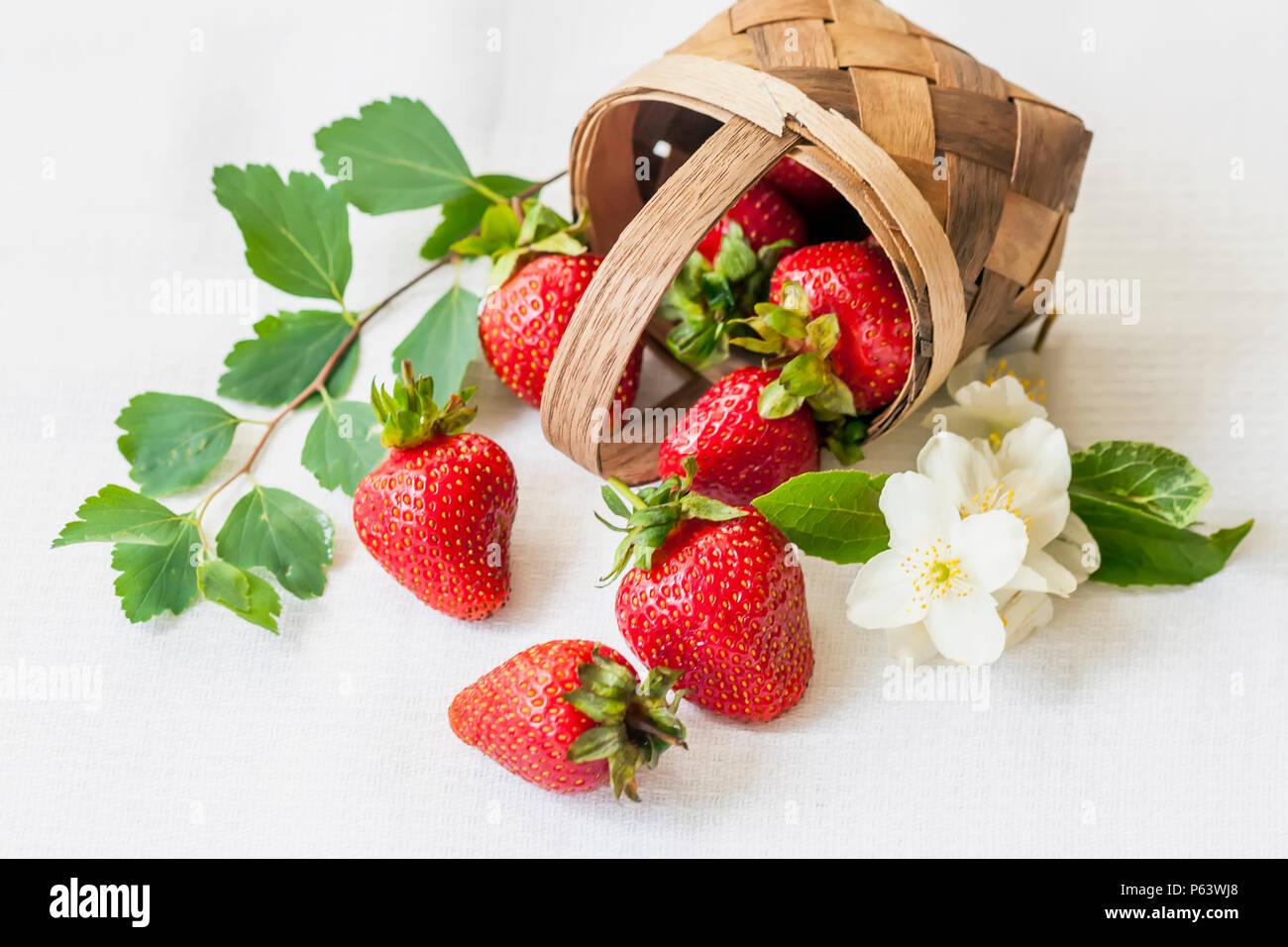 Miniature reclining basket with ripe strawberries, flowers, green foliage on light background. Concept of healthy food, detox, vitamins, dieting Stock Photo
