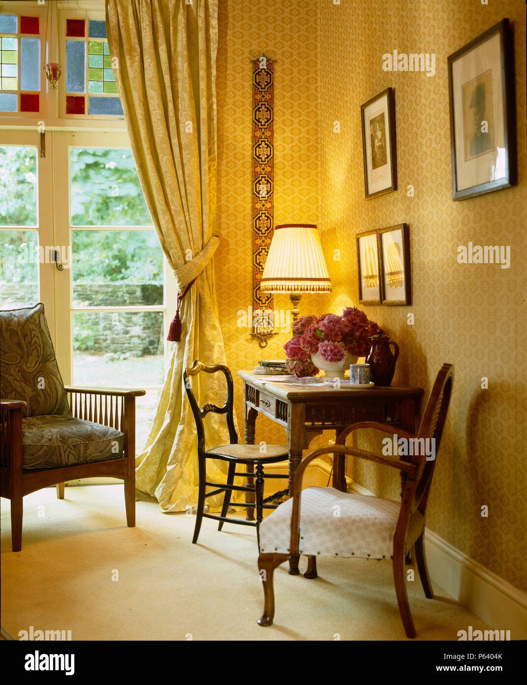 Corner of wallpapered room with brocade curtains and french windows to outside. Stock Photo