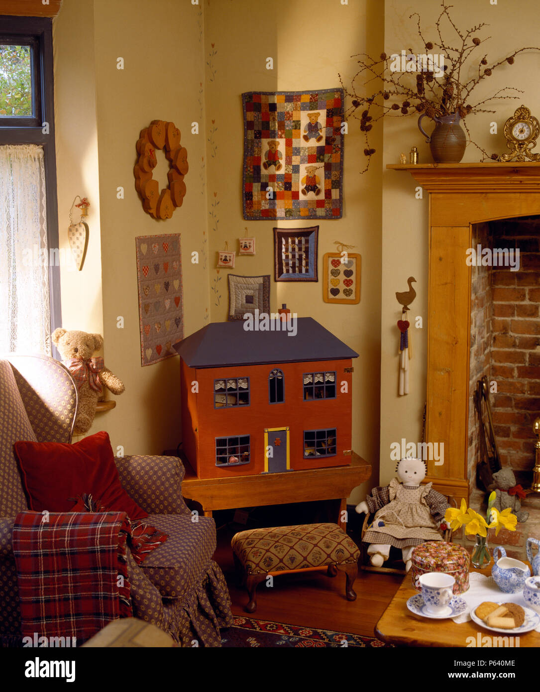 Simple doll's house beside armchair with plaid throw in small cottage living room Stock Photo