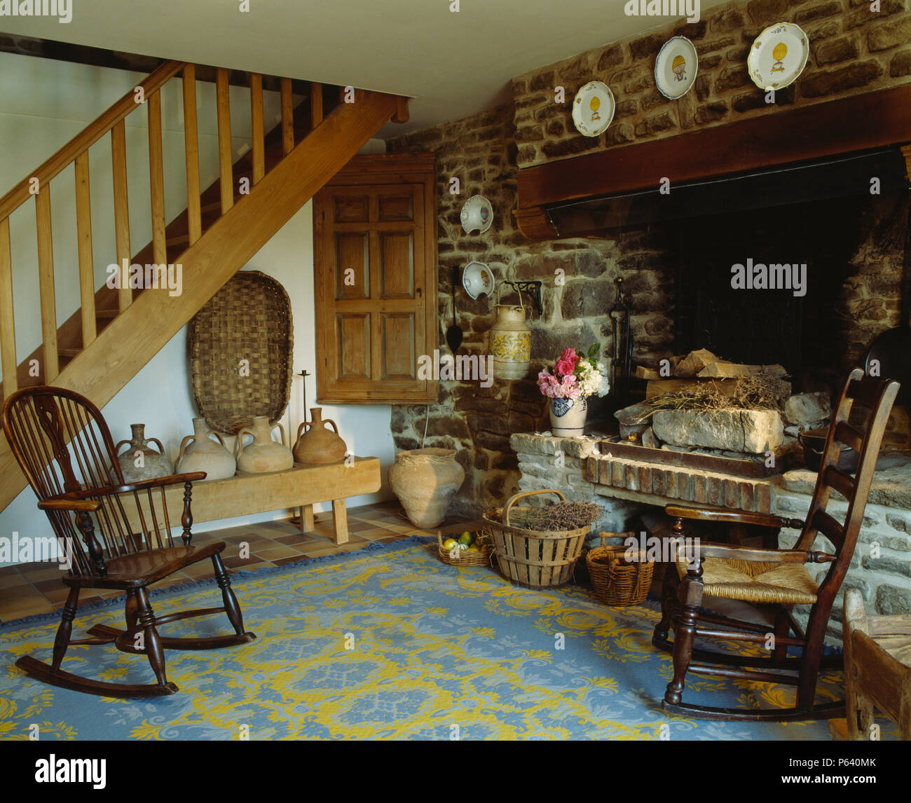 Antique rocking chairs beside inglenook fireplace in hall living room with wooden stairs and patterend blue carpet Stock Photo