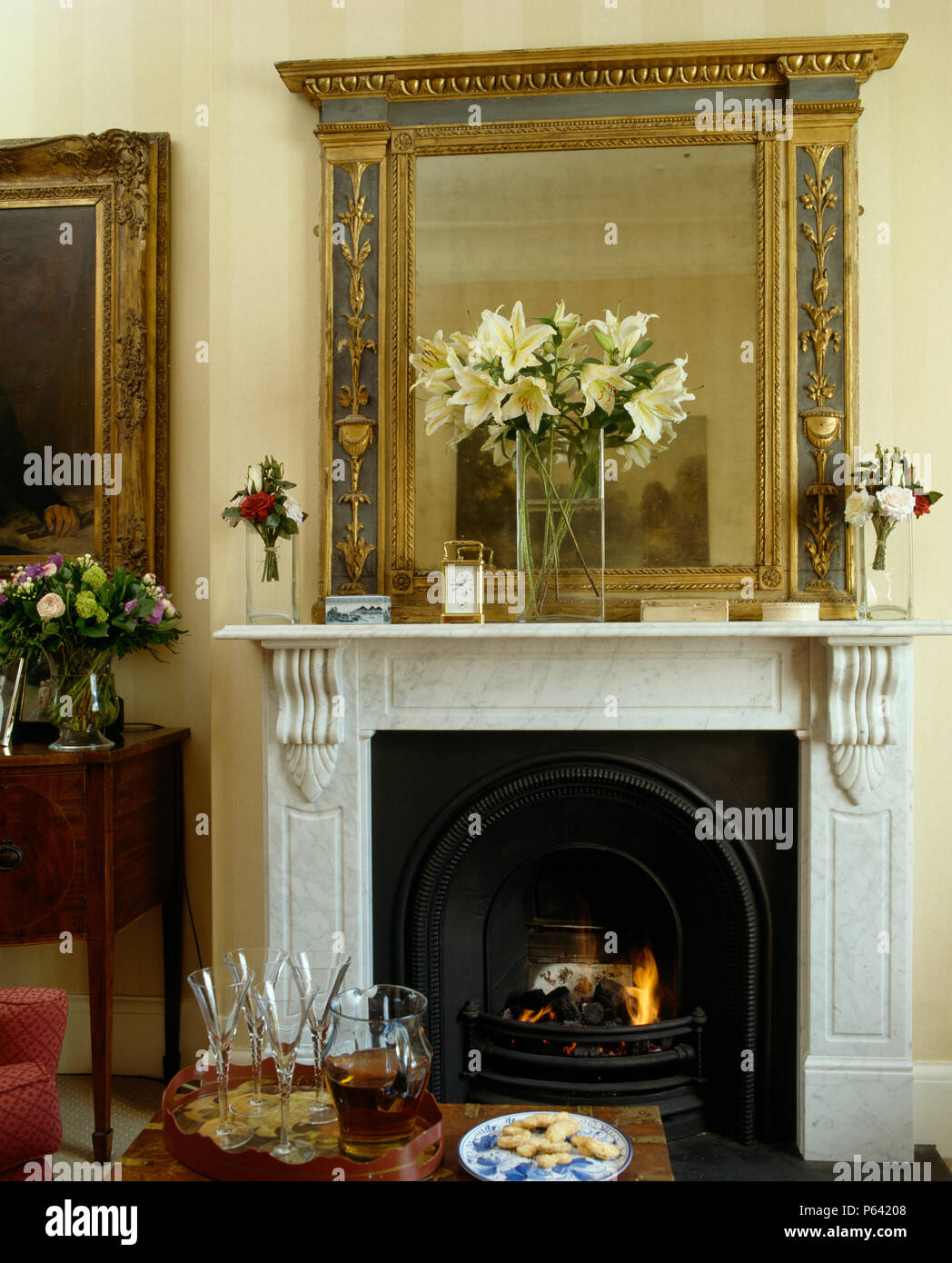 Antique mirror above marnble fireplace and lighted fire in traditional sitting room Stock Photo