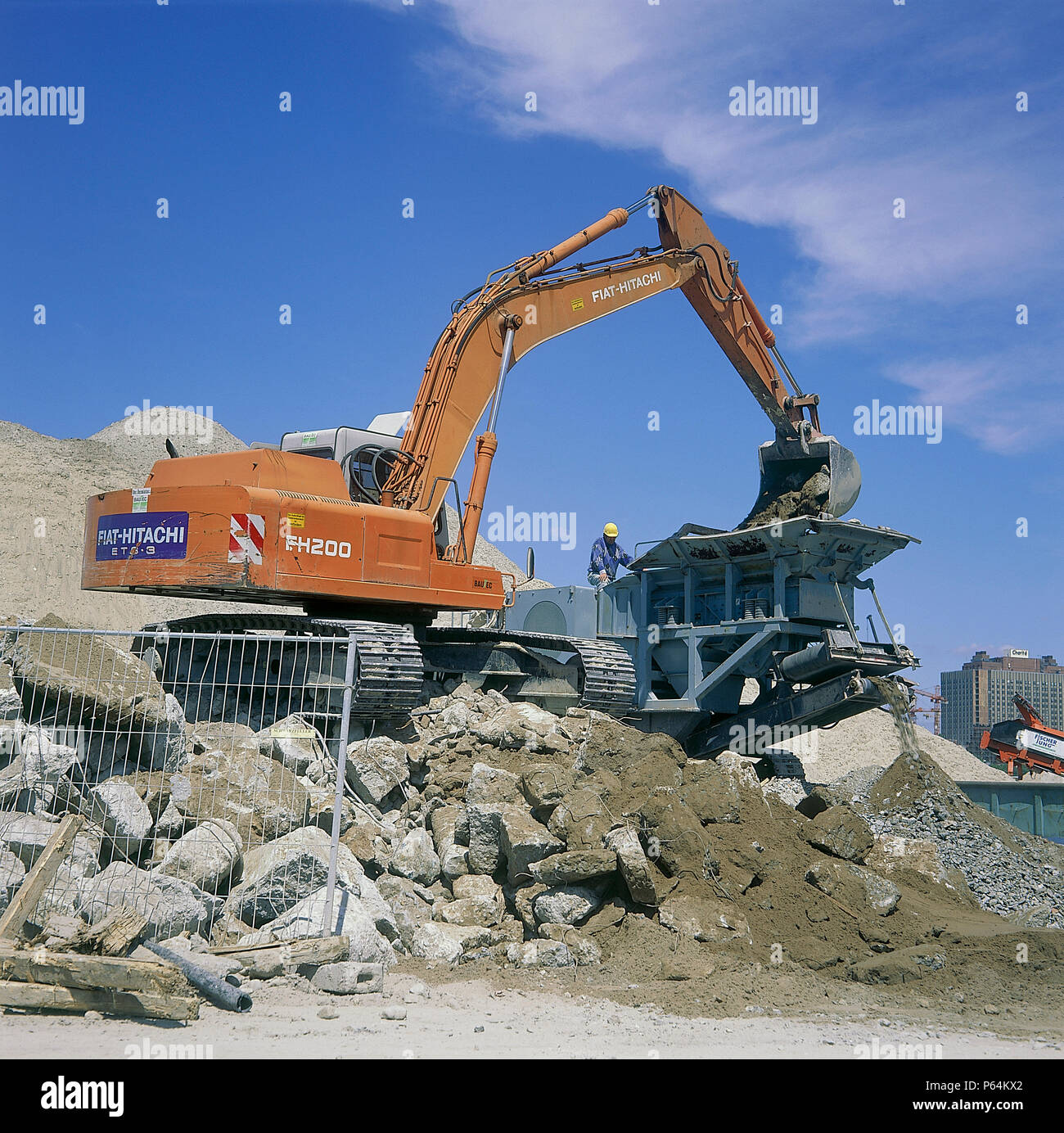 Fiat-Hitachi FH200 excavator loading concrete into mobile crusher for recycling. Stock Photo