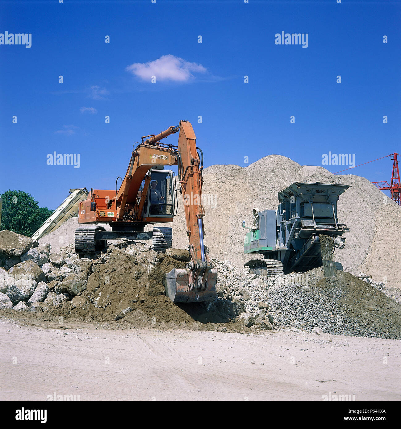 Fiat-Hitachi FH200 excavator loading concrete into mobile crusher for recycling. Stock Photo