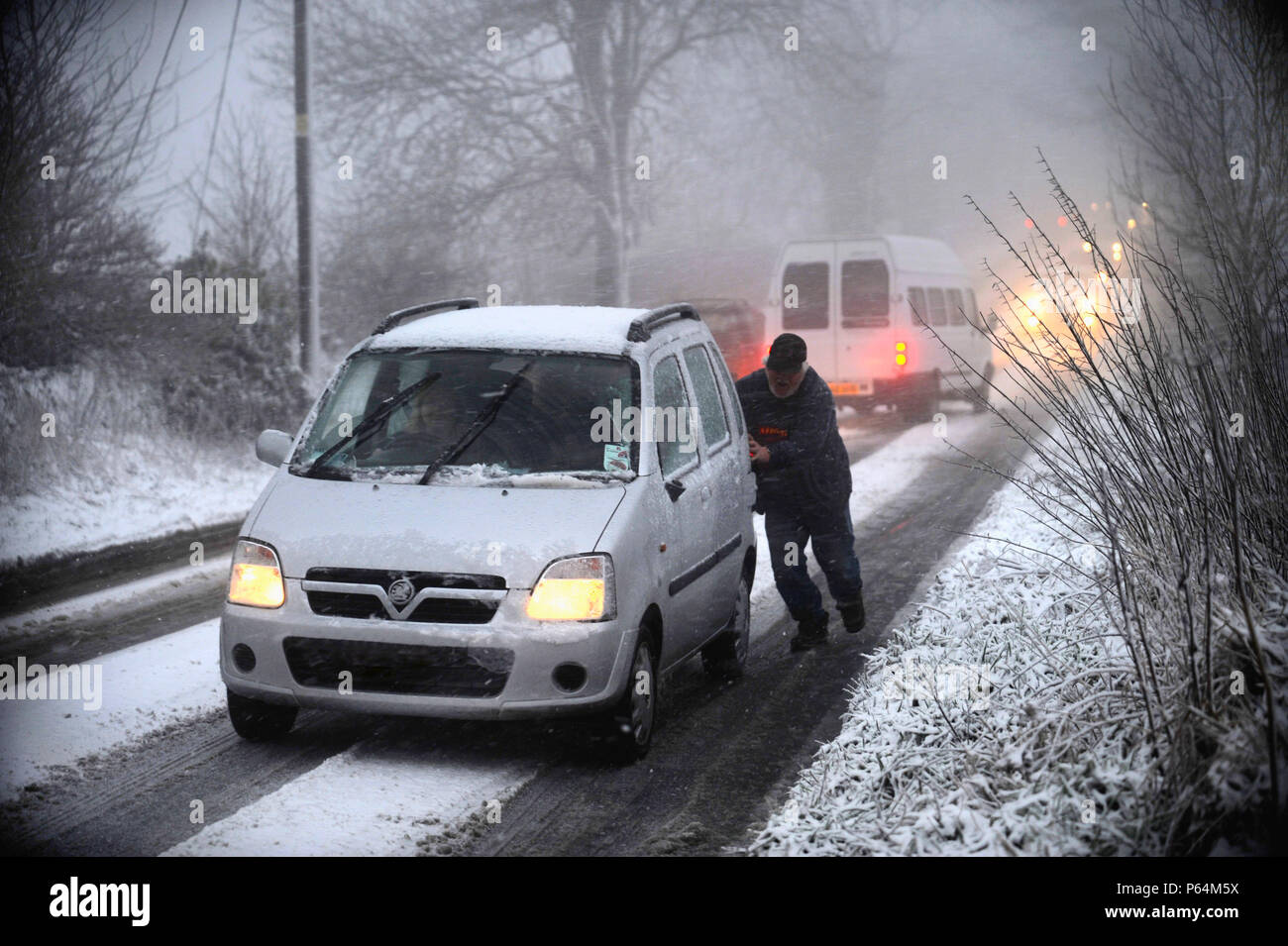 Man pushing car stuck on snowy road, UK Stock Photo