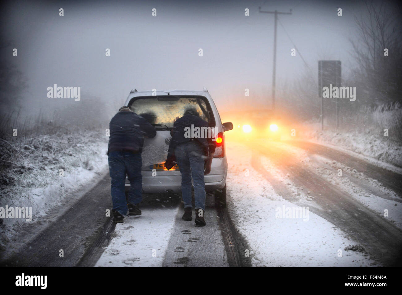 Men pushing car stuck on snowy road, UK Stock Photo