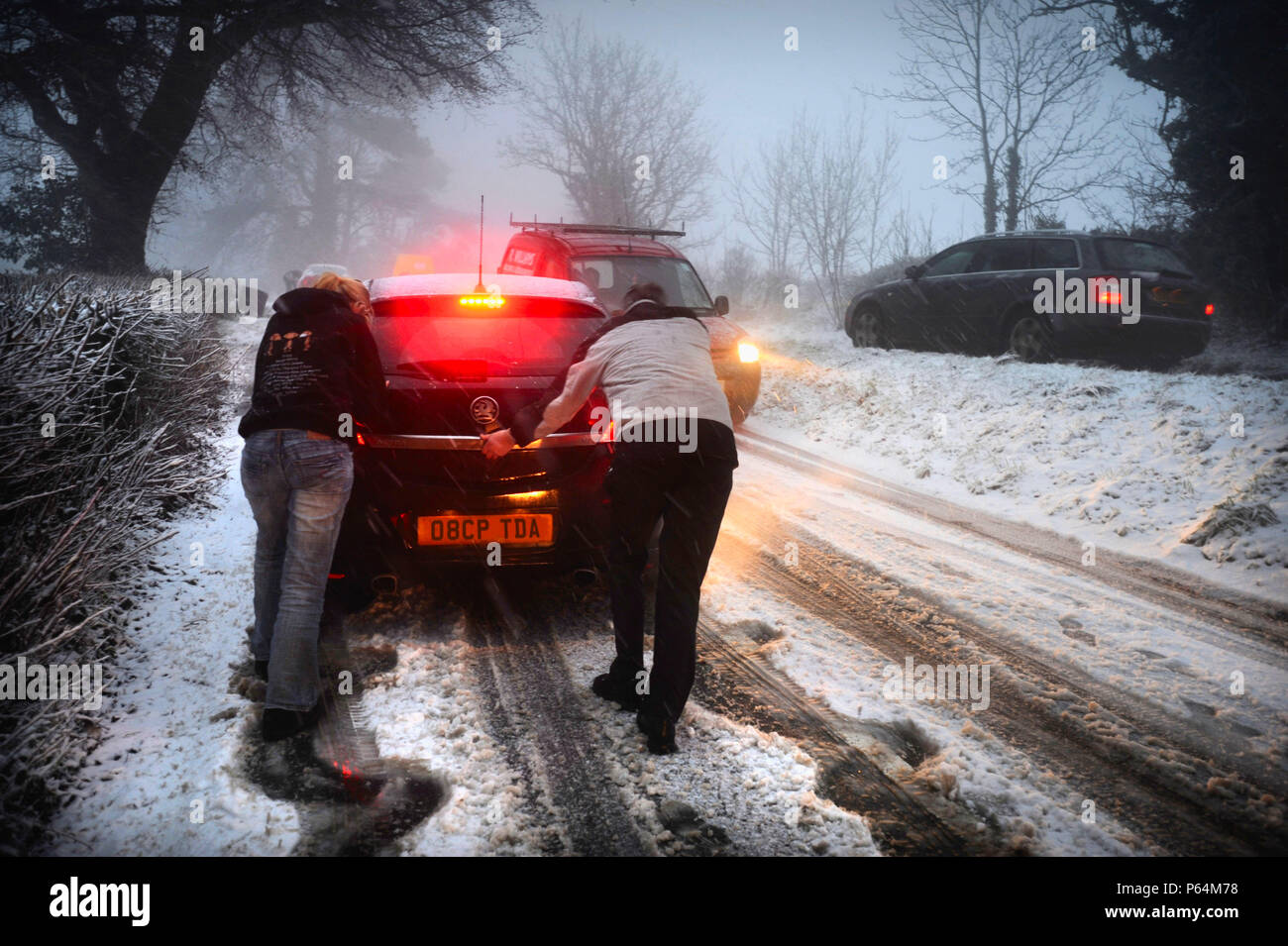 People pushing car stuck on snowy road, UK Stock Photo