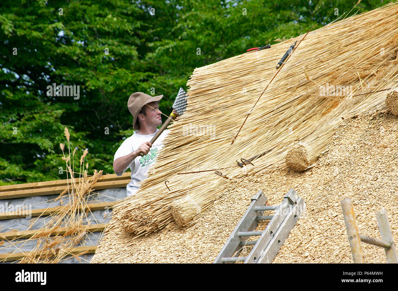 Male thatcher with hat working on a thatched roof in Co. Mayo, Ireland ...