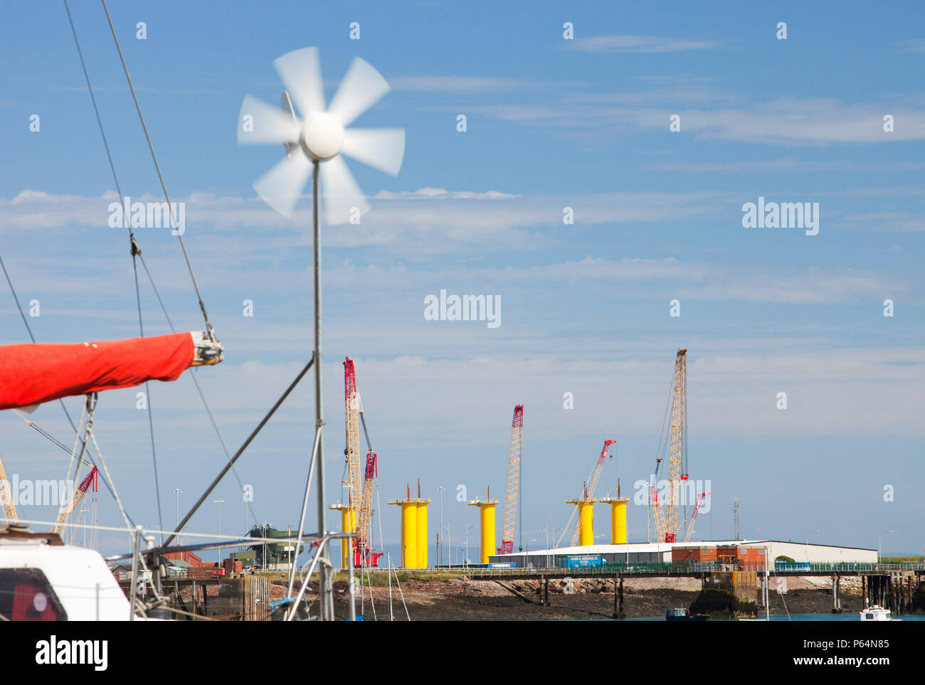 A yacht with a small wind turbine in front of the construction site for Dong Energy's offshore wind turbines. The yellow towers are the foundations fo Stock Photo
