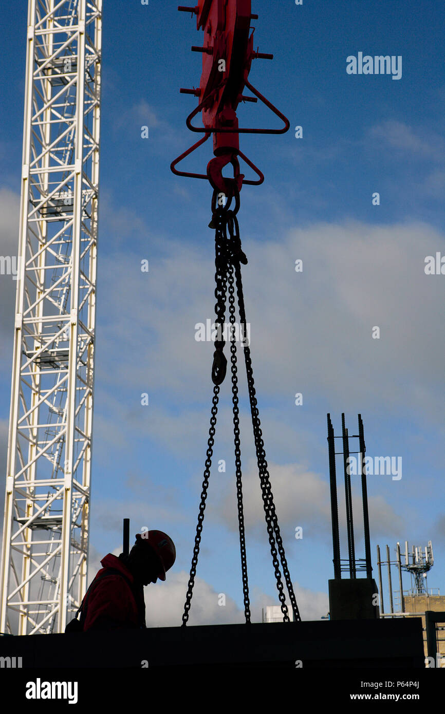Tower cranes with silhouette of a construction worker and pulley lifting attachment. Stock Photo