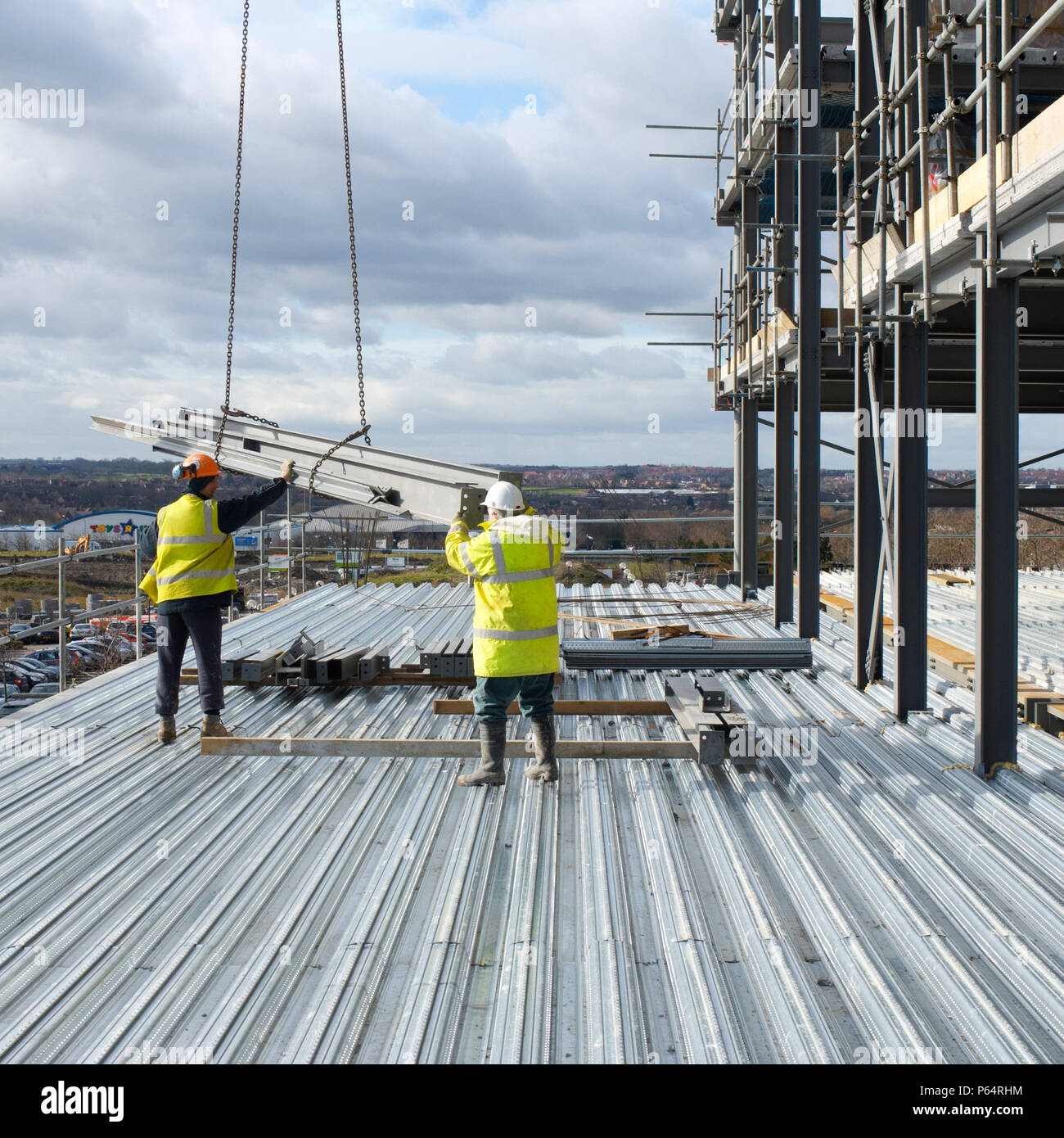 Construction workers receiving steel beams by crane at construction of