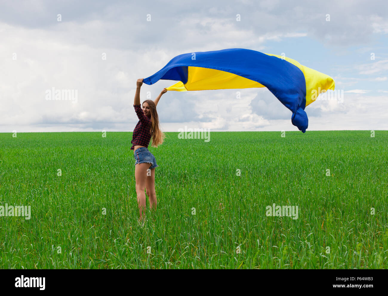 young beautiful ukrainian girl with an excellent figure in short jeans shorts holds a national Ukrainian yellow blue flag developing in the wind again Stock Photo