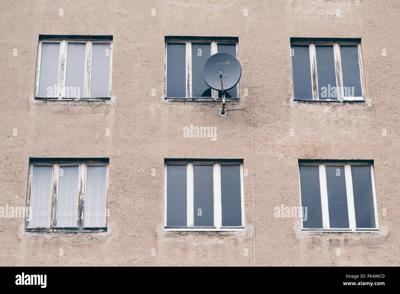 Ein hellbraunes herunter gekommenes Nebengebäude mit verschimmelten Fensterrahmen und Parabolantenne bei der Prora auf Rügen in Deutschland. Stock Photo