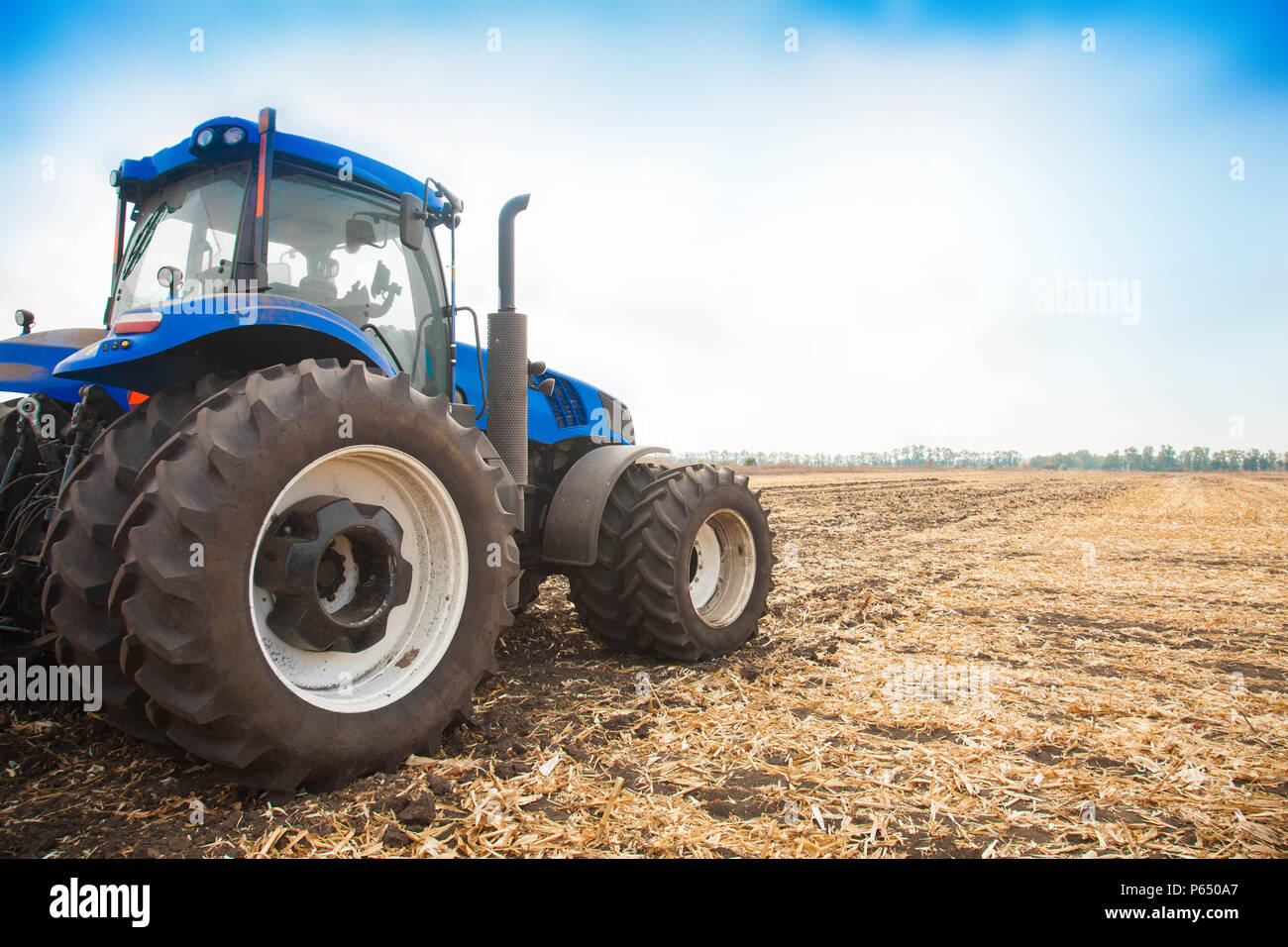 Blue tractor on the background of an empty field and a clear blue sky