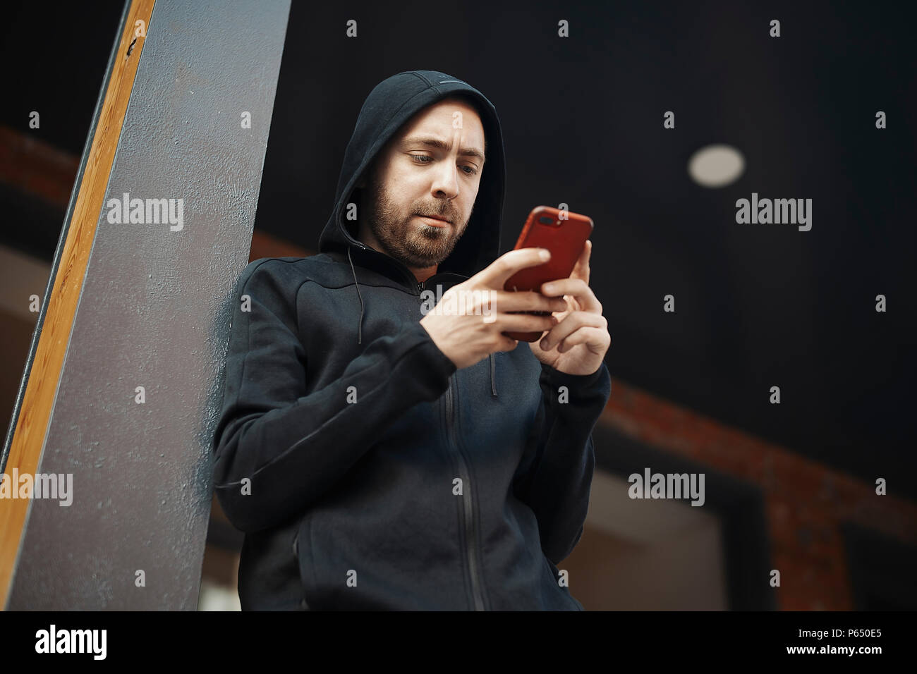 Bearded man standing next to concrete post and staring at the screen. Stock Photo