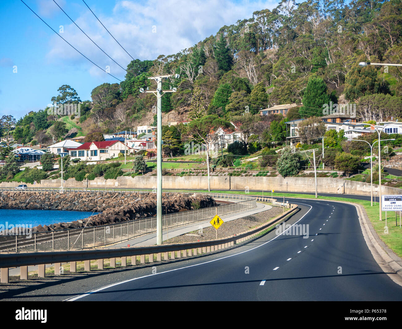 Asphalt road on coastline in Burnie with residential houses in distance. Burnie is a port city on the north-west coast of Tasmania, Australia. Stock Photo